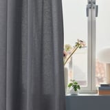 Finestra amb cortines VÄXELBRUK grises, flors roses en gerro.