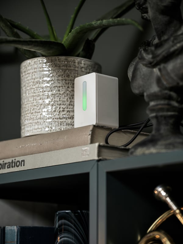 Un sensor de qualitat de l'aire blanc i elegant descansa sobre llibres apilats, mostrant llum verda.