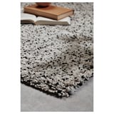 Primer pla de l'elegant catifa VINDUM amb taques negres en blanc, pila suau i gruixuda, llibres a la part superior.