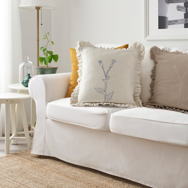 White ÅKERNEJLIKA embroidered cotton cushion with blue flowers on sofa.