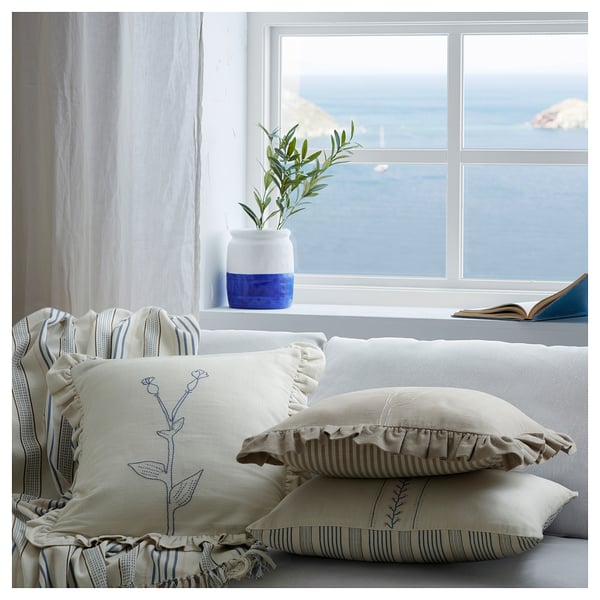 Cozy white sofa with blue striped pillows, embroidered, and a vase on the window.