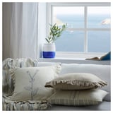 Cozy white sofa with blue striped pillows, embroidered, and a vase on the window.