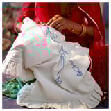 Woman in red dress hand-embroidering white, ruffled cushion cover with blue patterns.