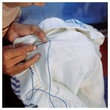 Person hand sewing white IKEA ÅKERNEJLIKA cushion cover with blue thread.