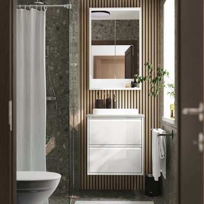 Modern white ÄNGSJÖN bathroom with sleek wash-stand, marble sink, frameless mirror, and wooden slats.