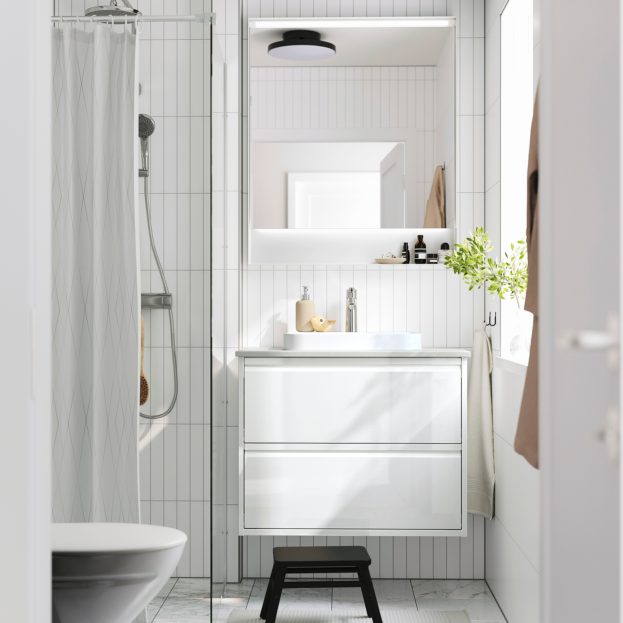 Modern bathroom: white cabinet sink, wall-mounted, black stool, glass shower, towels, plants.