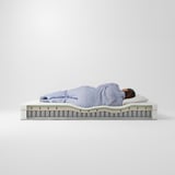 A person sleeping on a firm, white ÅNNELAND mattress with comfort zones and memory foam.