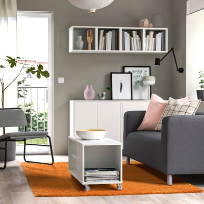 Modern living room with white rug, grey couch, wooden chair, white cabinet, and bookshelves.