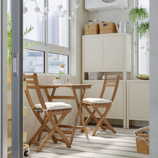 Small wooden ASKHOLMEN dining set with cushions by window, fitting in limited space.