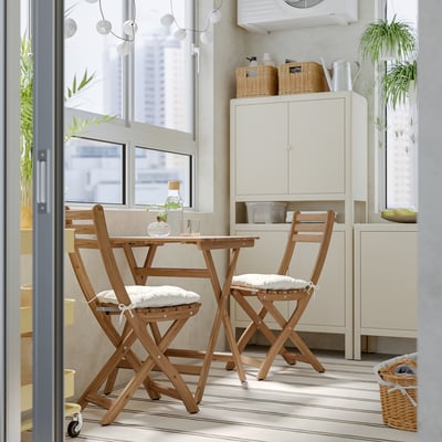 Small wooden ASKHOLMEN dining set with cushions by window, fitting in limited space.