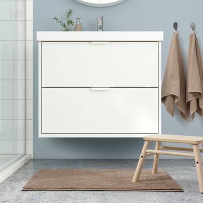 Modern bathroom with white vanity, beech stool, tan rug, & towels on hooks. Mat matches rug.