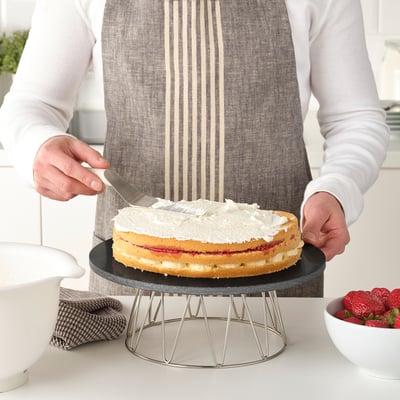 A person ices a cake on a rotating marble BAKGLAD stand, ensuring even coverage.