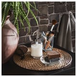 Bathroom counter with glass soap dispenser, small plants, makeup brushes, and a soap dish. Stone wall background.