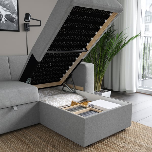 A grey sofa-bed with a storage chaise longue lifted to reveal pillows and board games inside.