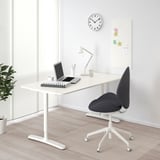 Minimalist home office: BEKANT desk, swivel chair, laptop, lamp, plant, whiteboard, clock.