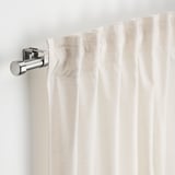 Window curtain rod with brackets and finials, holding creamy curtains.