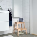 Minimalist bathroom with white tiled walls. Wooden BEKVÄM step stool holds blue towel & slippers.