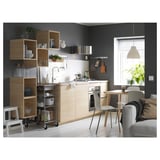 Modern kitchen with wood cabinets, white appliances, and gray sofa. Open shelves display dishes. Step stool, wooden chairs, window, and plant.
