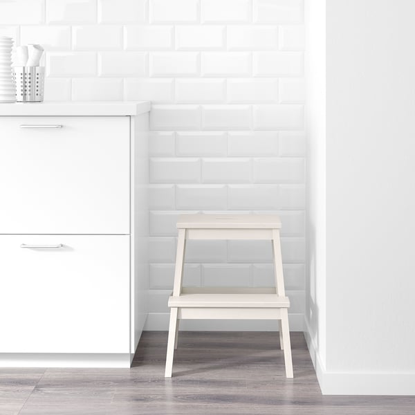 White wooden step stool by white cabinet, aids reaching high items.
