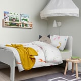Childs room with white BERGFINK duvet cover featuring giraffes, small bed, yellow blanket, cat pillow, bookshelf with books, and a small wooden stool.