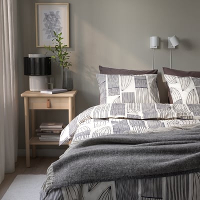 White BERGKORSÖRT duvet, minimalistic leaves, cotton-viscose blend. Nightstand with lamp, books, plant, gray wall.