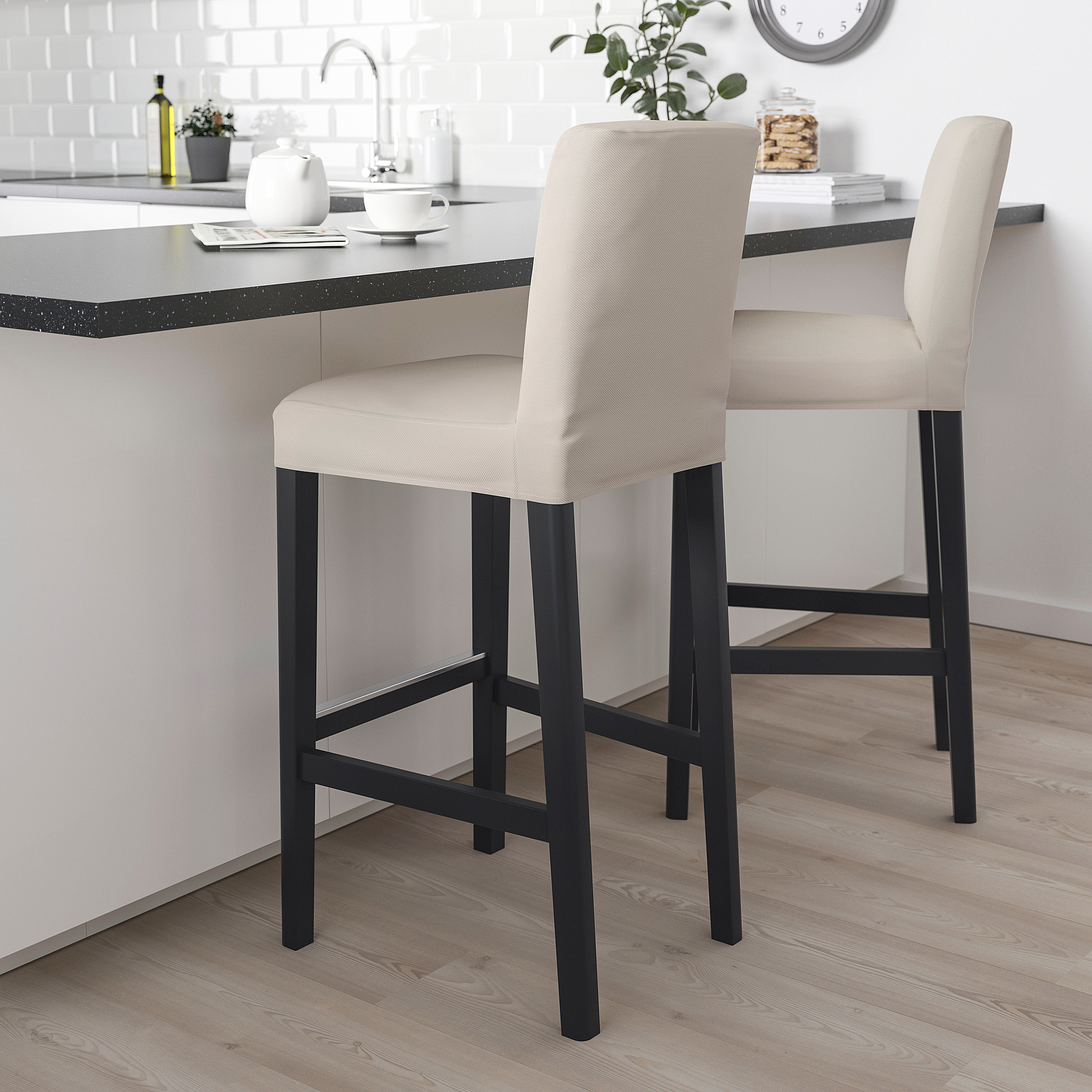 Two beige BERGMUND bar stools with black frames at white kitchen island.