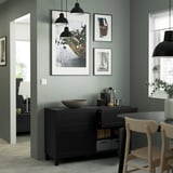 Modern dining room with dark wood sideboard, adjustable shelves, drawers, decor, and framed photos. Light green walls, large windows.