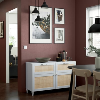 Stylish dining area with white and rattan sideboard, marble bowl, hanging lamps, and artwork. It is a prominent piece against burgundy wall.