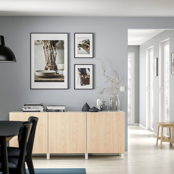 Modern living room with light wood cabinet, various vases, framed photos, and black dining chair.