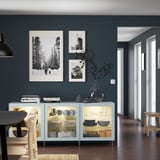 A modern dining room a light blue BESTÅ sideboard against grey walls. The sideboard holds dishes and decor. Black and white photos hang above it.