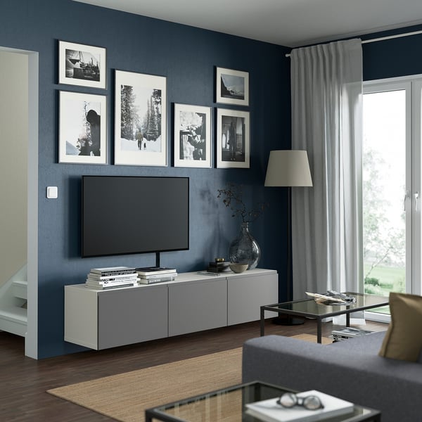 Modern living room with BESTÅ white tv bench, sleek design, wooden floor, grey walls, large flat screen tv, black and white photos, clean aesthetic.