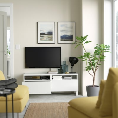 Modern living room with BESTÅ tv unit, yellow chairs, natural rug, and plant.