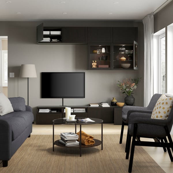 Modern living room with gray sofa, armchair, and tv storage. Includes wall-mounted cabinets and a glass coffee table with books and candles.