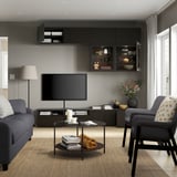 Modern living room with gray sofa, armchair, and tv storage. Includes wall-mounted cabinets and a glass coffee table with books and candles.