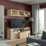 Modern living room with burgundy walls, wooden tv stand, glass cabinets, flat-screen tv, and natural light.