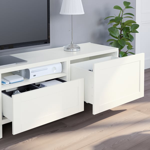 White BESTÅ tv stand with adjustable shelves, open drawer, and cable management. A lamp and plant decorate the top.