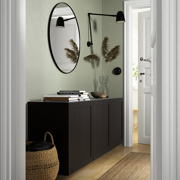 Modern hallway with BESTÅ unit, black cabinet against green wall, mirror, books, and decor.