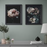 Two framed floral art prints hang above a console table displaying a lamp, vase, and plant.