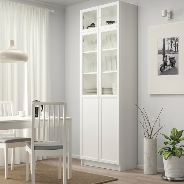 Modern dining room with BILLY bookcase, displayed plates, round table, scooter photo, plant, and pendant light.