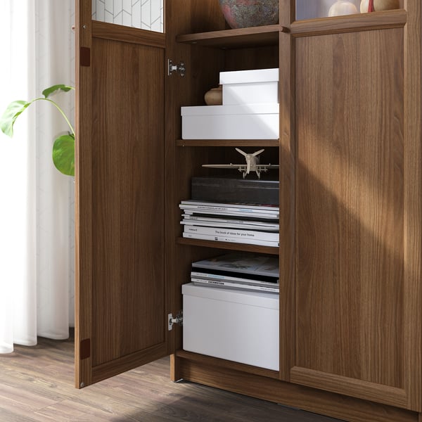 Wooden cabinet BILLY with open door revealing shelves storing boxes, books, and a model airplane.