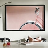 Pink bicycle with white seat, soft pink background, table with glass, candle holders, book, cushions.