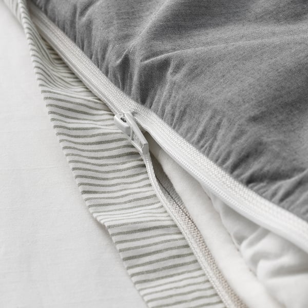 Close-up of a neatly made bed with a zippered white cotton duvet cover, showing crisp, cool fabric and striped detail.