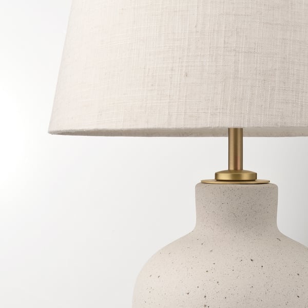 Modern table lamp with a textured cream base, brass accents, and a white fabric shade, exuding a warm, inviting glow.