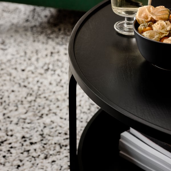 Black round coffee table with storage. Bowl of dried fruits and wine glass on top. Speckled countertop beneath.