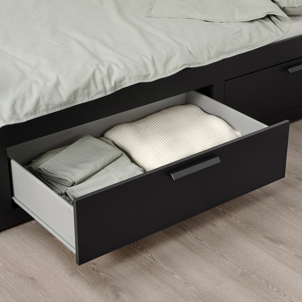 Open drawer of BRIMNES day-bed, showing folded sheets and pillows, used for storage under bed base.
