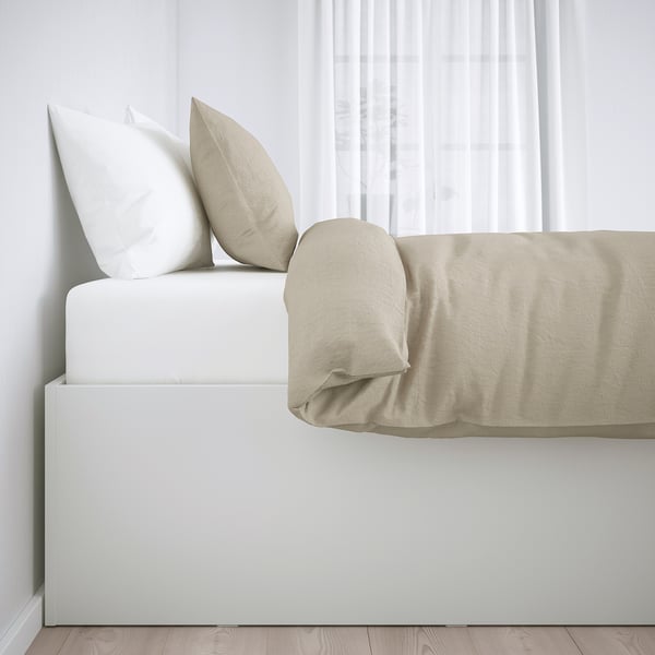 Minimalist bed with beige cover and two pillows, offering hidden storage under the slatted base. Ideal for extra bedding.