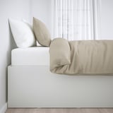 Minimalist bed with beige cover and two pillows, offering hidden storage under the slatted base. Ideal for extra bedding.