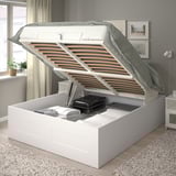 White ottoman bed with slatted base revealing storage with blankets. Near grey wall art.
