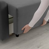A person transforming a sofa into a bed by pulling out a section, showcasing its storage function.