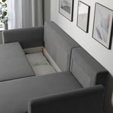 Modern gray sofa bed by BRISSUND, shown with hidden bedding compartment open, ideal for guest sleeping.